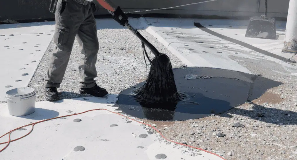 Roofing worker applying waterproof coating on flat roof surface.
